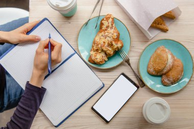 Kadın kafedeki defterine kahve ve fırınla yazı yazıyor.