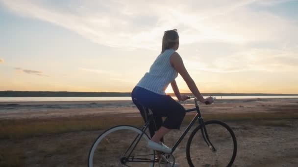 Hipster menina andar de bicicleta ao pôr do sol — Vídeo de Stock
