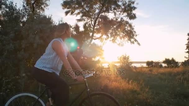 Csípő lány lovaglás kerékpár naplementekor — Stock videók