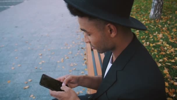 若いファッション黒スーツのアフリカ系アメリカ人男性と夏に路上で電話を使用して帽子 — ストック動画