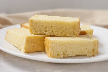 Açık gri bir zemin üzerinde beyaz bir tabakta keten peçeteyle taze pişmiş mısır ekmeği dilimleri..