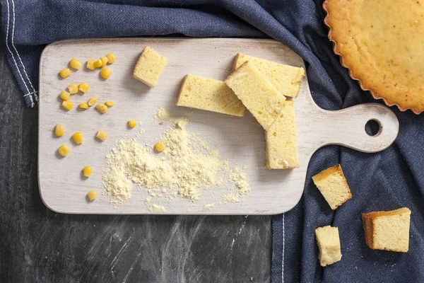 Pane di mais appena sfornato su un'asse bianca di legno con grano e farina su uno sfondo scuro con un tovagliolo. Pasticcini tradizionali nella cucina nazionale statunitense. Vista dall'alto — Foto Stock