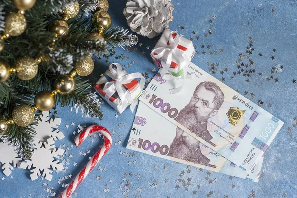 Yıldızlar, hediyeler, kar taneleri, şekerler ve Noel ağacı olan mavi bir arka planda Ukrayna 1000 Hryvnia 'sı. Ukrayna 'da Noel ve Yeni Yıl hediyeleri alma kavramı
