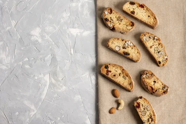 Traditional Italian cookie Biscotti or Cantuccini with hazelnuts, almonds, walnuts on a gray background with a beige linen napkin. Top view, copy space