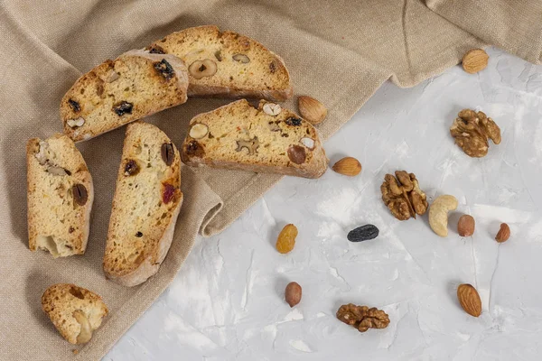 Geleneksel İtalyan kurabiyesi Biscotti ya da fındıklı Cantuccini, badem, fındık, bej keten peçete ve kuru portakal dilimleriyle gri bir zemin üzerinde ceviz.