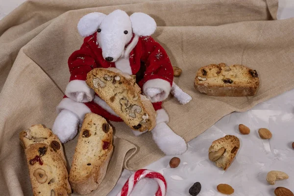 Традиционные итальянские печенье Biscotti или Cantuccini с фундуком, миндаль, грецкие орехи в руках белой крысы в костюме Санта-Клауса рядом с елкой. Christmas and New Year 's baking . — стоковое фото