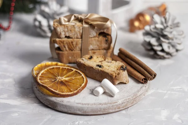 Biscoitos italianos tradicionais ou biscoitos cantuccini em uma tábua redonda de madeira branca com canela, fatias de laranja secas e marshmallows em um fundo leve com cones de pinho. Conceito de cozimento de Natal — Fotografia de Stock