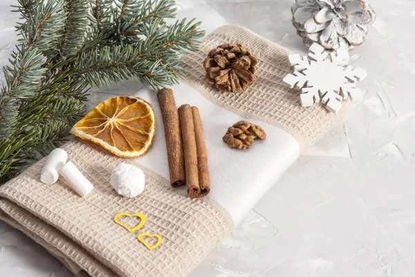 Cinnamon sticks on a beige napkin with slices of dried orange, pine cone, nuts, snowflakes and marshmallows near a fir branch. Christmas concept. Copy space.