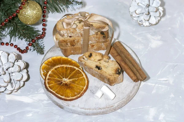 Traditionelle italienische Kekse oder Cantuccini auf einem runden weißen Holzbrett mit Zimt, getrockneten Orangenscheiben und Marshmallows auf einem hellen Tisch neben einem Weihnachtsbaum. Weihnachtsbäckerkonzept — Stockfoto