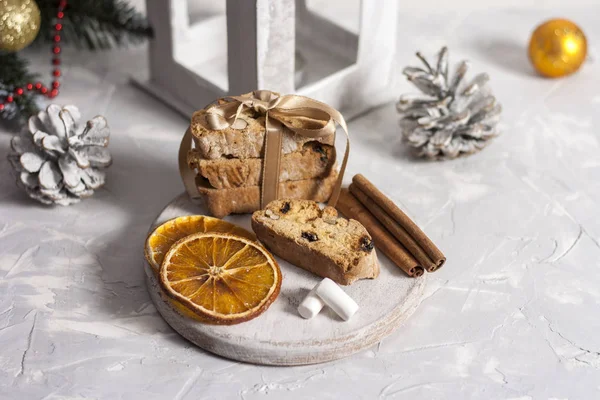 Traditional Italian biscotti or cantuccini cookies on a round white wooden board with cinnamon, dried orange slices and marshmallows on a light table near a Christmas tree. Christmas baking concept — Stock Photo, Image