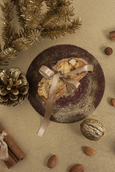 Traditional Italian biscotti or cantuccini cookies on a round white wooden board with cinnamon, dried orange slices and walnut in gold color near a Christmas tree branch. Christmas baking. Flat lay — Stock Photo, Image