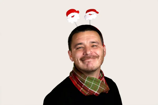 Фото счастливого молодого человека в черном свитере и красно-зеленый шарф в рождественских рогах с лицом Санта-Клауса на голове. Серый фон, пространство для копирования . — стоковое фото