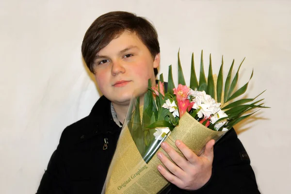 Young attractive guy in casual wear with a bouquet of flowers in holiday packaging. — Stock Photo, Image