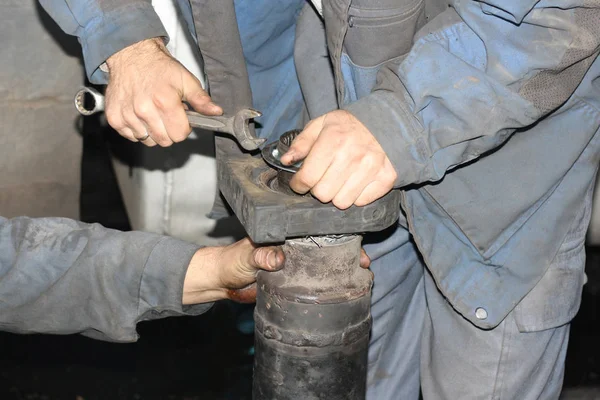 Truck repair. Two mechanics in work clothes are repairing wagon crankshaft with tools.