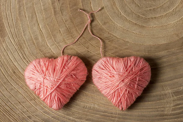 Dos corazones rosas hechos de hilos de lana sobre un fondo de madera tejido en un nudo . — Foto de Stock