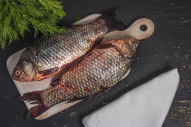 İki taze haç balığı, siyah ahşap arka planda beyaz bir tahta kesme tahtasının üzerinde yatar. Üst görünüm