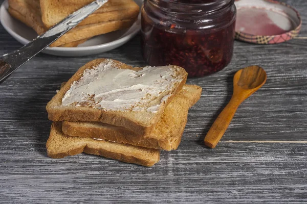 Ingredients for a delicious breakfast - toasted bread with butter and homemade raspberry jam on a wooden table — Stock Photo, Image