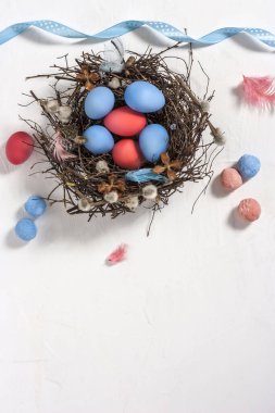 İnce dallı bir yuvaya boyanmış Paskalya bıldırcın yumurtaları ve kopyalanmış beyaz desenli arka plan tüyleri. Üst görünüm.