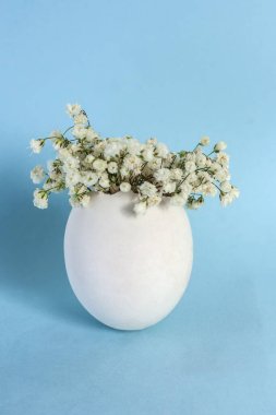 Asgari paskalya konsepti. Açık mavi arkaplanda bir buket narin çiçekli beyaz yumurta ve fotokopi alanı. Dikey yönelim.