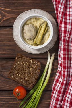 Bir tabak patates püresi buharda pişmiş pirzola ve ahşap bir zeminde salatalık turşusu. Dikey yönelim.