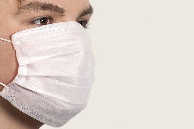 Corona virüsü. Beyaz arka planda maskeli genç bir adam. Virüslere, enfeksiyonlara, egzoz dumanlarına karşı koruma