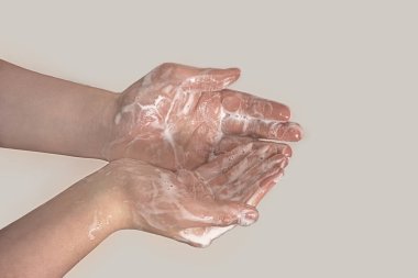 Gri arka planda sabun köpüğü giymiş genç bir adamın elleri. El yıkama. Minimum hijyen, virüs koruma konsepti