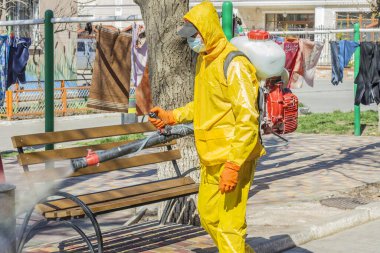 Ukrayna, Odessa, 2020 baharında. Coronavirus. Sarı takım elbiseli ve maskeli temizlik işçisi, Coronavirus 'a karşı basınç altında alkol solüsyonuyla sokakları yıkıyor. Koruma
