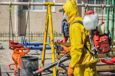 Ukrayna, Odessa, 2020 baharında. Coronavirus. Sarı takım elbiseli ve maskeli temizlik işçisi, Coronavirus 'a karşı basınç altında alkol solüsyonuyla sokakları yıkıyor. Koruma