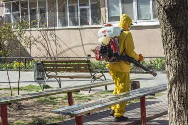Ukrayna, Odessa, 2020 baharında. Coronavirus. Sarı takım elbiseli ve maskeli temizlik işçisi, Coronavirus 'a karşı basınç altında alkol solüsyonuyla sokakları yıkıyor. Koruma