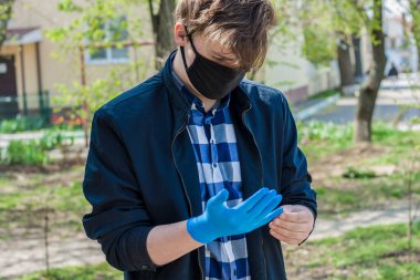 Young guy wears sterile blue disposable rubber gloves outdoors on a sunny day clipart