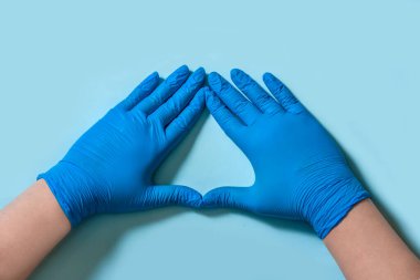 Kalp, mavi kauçuk eldivenli eller açık mavi arka planda.