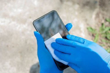 Koronavirüs enfeksiyonunun yayılmasını önlemek için. Kapatın elleri lastik mavi eldivenler akıllı telefonu dezenfekte ediyor..
