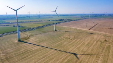 Nauen, Brandenburg / Almanya - 26.03.2020: Güneşli havada bir yolda iki rüzgar türbini, bir tarlaya düşen gölgeyi ve dolayısıyla olası çevresel etkiyi net bir şekilde görebilirsiniz.