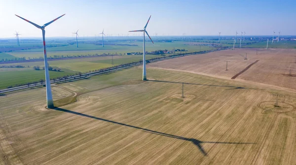 Nauen, Brandenburg / Almanya - 26.03.2020: Güneşli havada bir yolda iki rüzgar türbini, bir tarlaya düşen gölgeyi ve dolayısıyla olası çevresel etkiyi net bir şekilde görebilirsiniz.