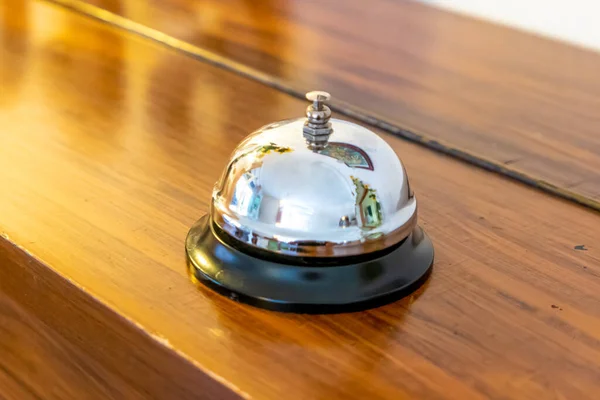 A chrome-plated table bell or reception bell with black base on a wooden surface that reflects and shines in the light