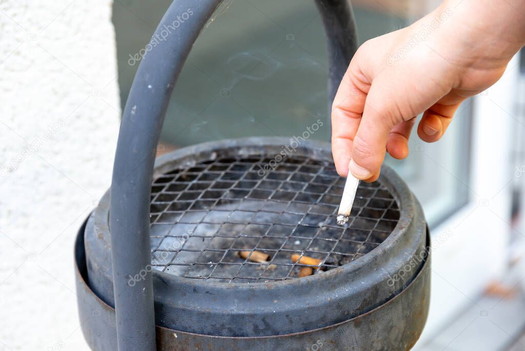 Berlin, Berlin/Germany - 03.09.2019: A hand extinguishing a cigarette in a black standing ashtray with handle and a sieve