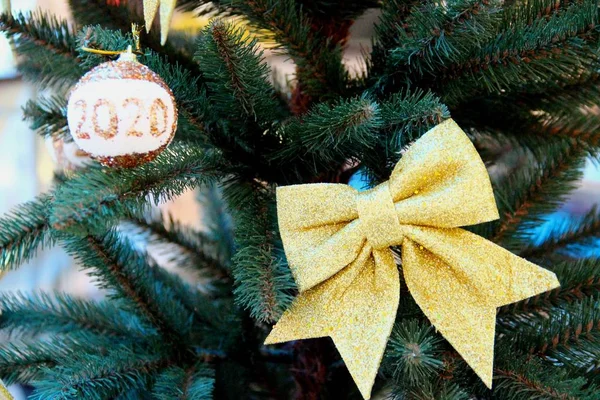 Nya år leksaker Gyllene båge och guld boll med vit insats inskrift 2020, på bakgrunden av grenarna av den konstgjorda gröna julgran — Stockfoto