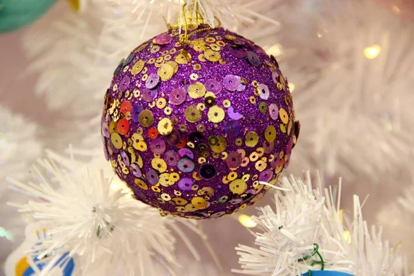 violet Christmas ball in gold sequins against the background of white artificial spruce. concept of Christmas toys and balls