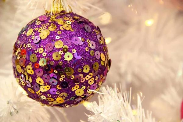 Фиолетовый рождественский шар в золотых блёстках на фоне белой искусственной ели. Концепция рождественских игрушек и мячей — стоковое фото