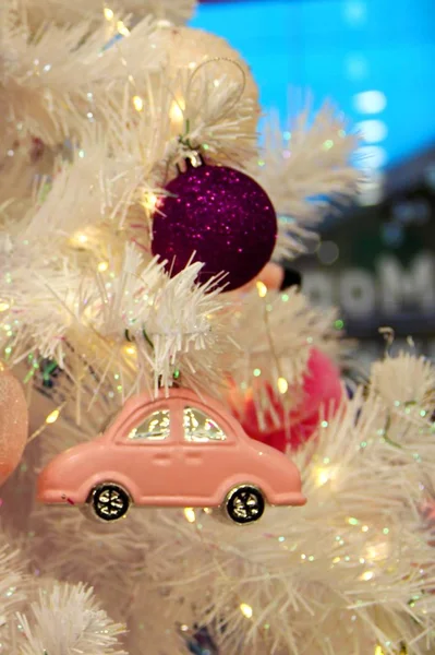 Розовый игрушечный автомобиль на фоне ветвей белой искусственной ели и фиолетового стекла новогодний шар. Рождественский фон — стоковое фото