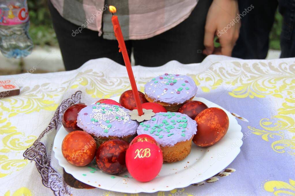 Orthodox Easter, preparation for consecration with Holy water. Easter cakes with a candle and colorful Easter eggs on background elements of human bodies without faces. 