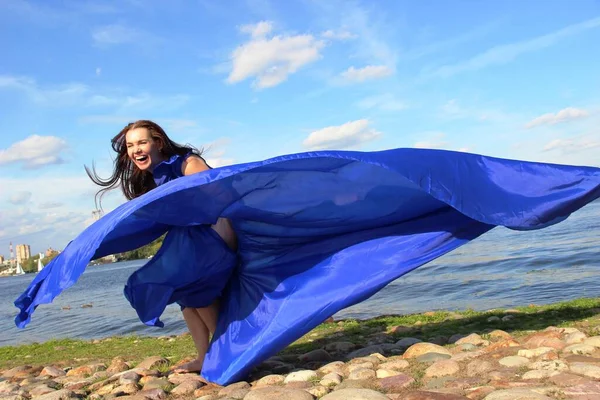 Femme dans une longue robe bleue qui flottait dans le vent. rire bruyamment brune. promenade le long de la rivière . Images De Stock Libres De Droits