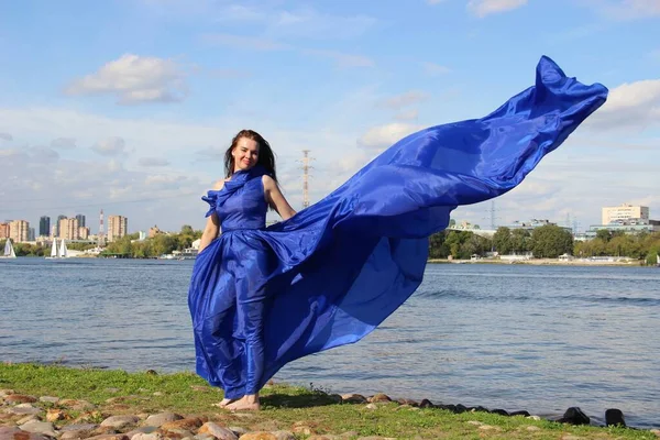 Mujer en un vestido azul largo que revoloteaba en el viento. Río —  Fotos de Stock