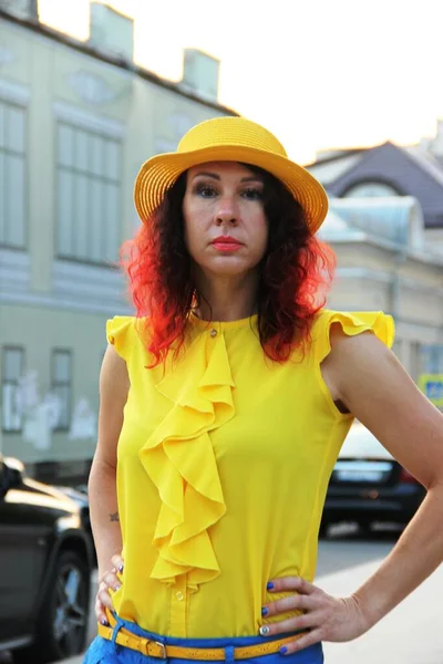 Mujer de pelo rizado rojo, blusa de seda amarilla y sombrero amarillo. una mujer en la calle por la noche. Retrato en un entorno urbano — Foto de Stock