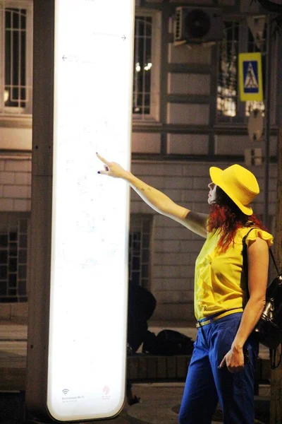 Mujer joven con un sombrero amarillo mira el mapa electrónico de la ciudad. Noche en Moscú y concepto turístico —  Fotos de Stock