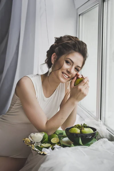 Beautiful girl eats fruit sitting by the window sill 8750. — Stock Photo, Image