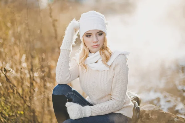 Winter portrait of a girl sitting on a large stone beside the ro — Stock Photo, Image