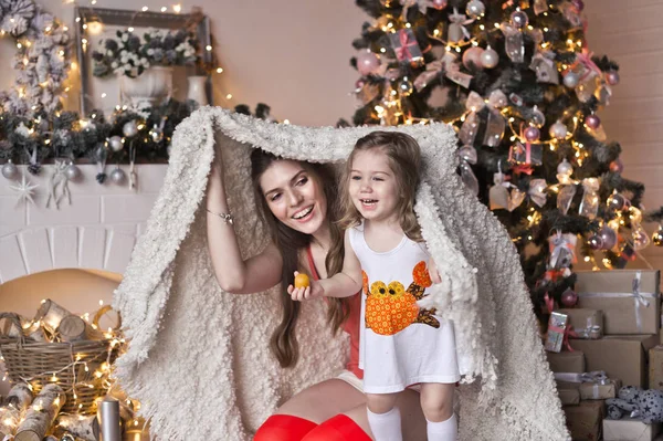 Mãe e filha se esconderam sob um cobertor perto da árvore de Natal — Fotografia de Stock
