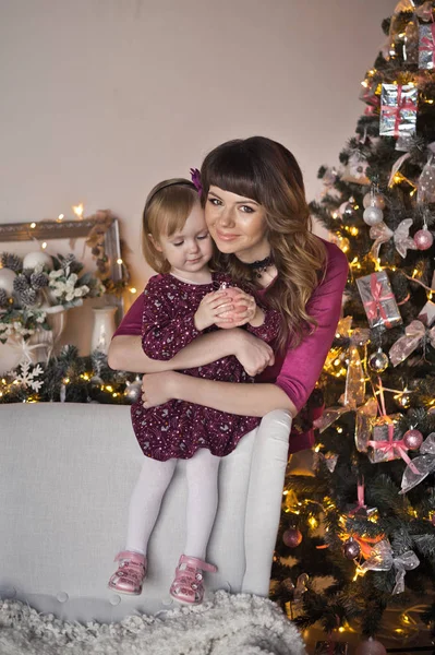 Mamá está abrazando a su hija en el fondo del árbol de Navidad — Foto de Stock