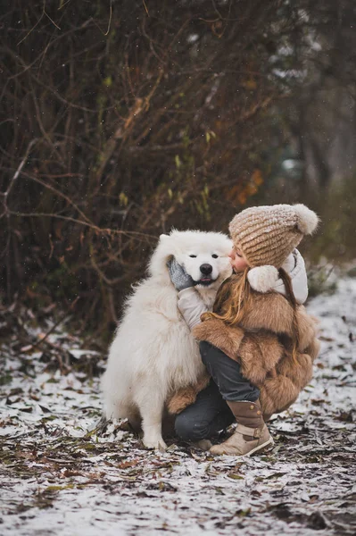 Ein Kind umarmt und streichelt seinen weißen zotteligen Hund. — Stockfoto